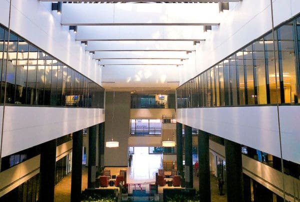 View from a high floor showing the interior of a modern commercial building with expansive glass walls, revealing open office spaces and contemporary interior design.