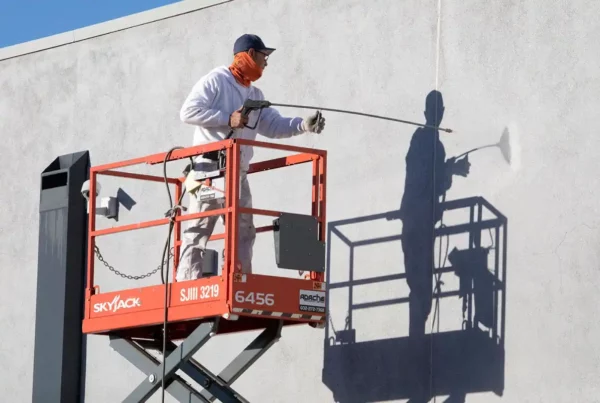 Painter using a lift to spray paint on the exterior of a building.