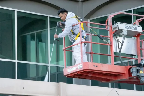 Painter on a lift spraying paint on a building's exterior.