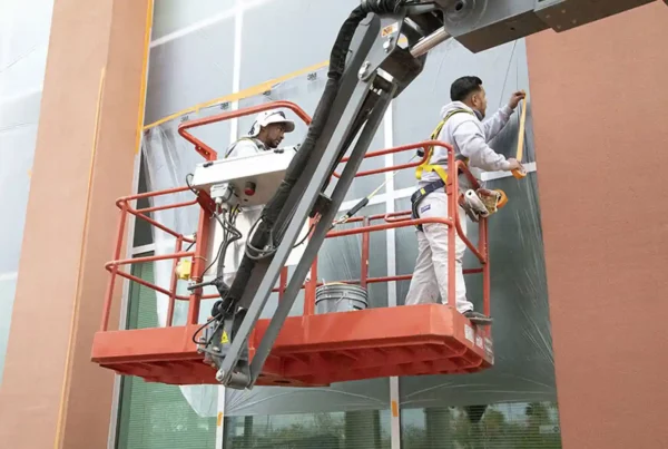 Painters on a lift preparing windows for repainting the exterior of a building, ensuring meticulous preparation and attention to detail.