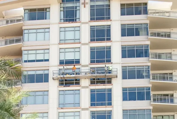 A painter using safety equipment to work on painting a glass building, emphasizing safety and precision in their task.